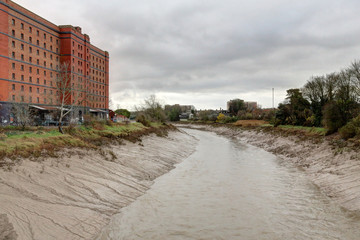 The river Avon waters with mud just after a storm, next to a red brick abandoned industrial building in a cloudy winter day in Bristol, United Kingdom
