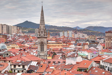 Fototapeta na wymiar A landscape of Bilbao mountains and city centre with clouds, mountains, houses roofs and the cathedral belltower at sunset, in Vizcaya, Spain