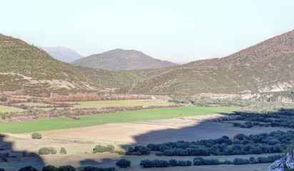 A landscape of rocky mountains and crop fields with Santa Maria y la Peña rural town, as seen from Mallos de Riglos, in the Pyrenees, Aragon, Spain