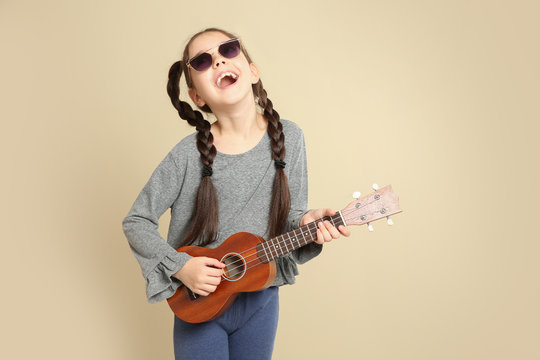 Portrait of little cheerful girl playing guitar on color background