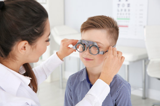Children's doctor putting trial frame on little boy in clinic. Eye examination