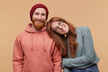 Indoor shot of cheerful redhead woman, keeps her hand on boyfriend shoulder, smiles and feels happy. family album image of Caucasian couple enjoy their partnership. Isolated over biege background