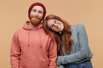 Indoor shot of cheerful redhead woman, keeps her hand on boyfriend shoulder, smiles and feels...