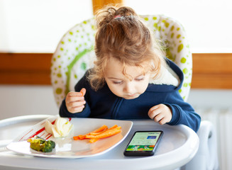 Toddler eats while watching movies on the mobile phone.