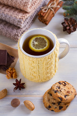 Knitted yellow cup with tea drink, cookies, cinnamon, winter decorations. Warm and cozy atmosphere while cold season