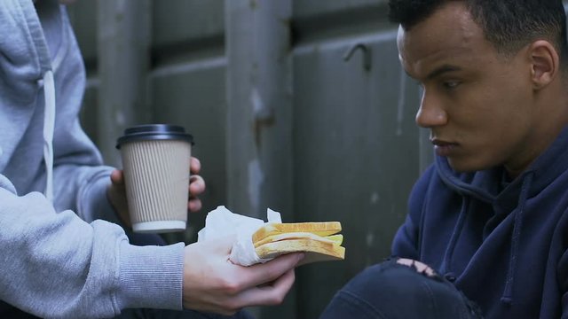 Kind boy sharing tasty sandwich and warm coffee with gamin, human compassion