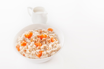 Oatmeal with pumpkin and nuts in a plate and a jug with milk on a white background. Close-up. Copy space