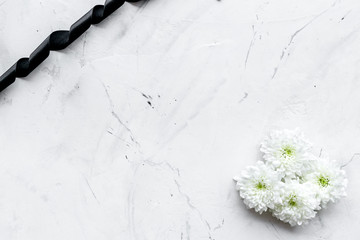 Funeral symbols. White flower near black ribbon on white stone background top view space for text
