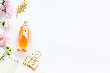 Perfume on feminine desk. Women's accessories. Perfume near notebook for dairy among flowers on...