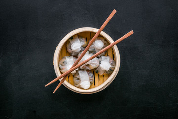 Chinese food set with dim sum, sticks on black background top view