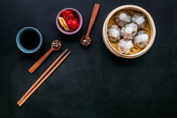Chinese food set with dim sum, sticks and tea on black background top view copy space