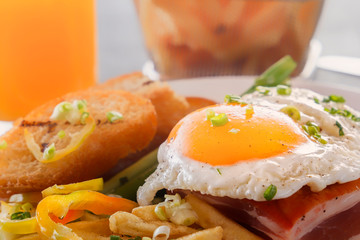 Fried egg with bacon in a plate with fried pieces of bread, greens and french fries on a gray wooden table. Close-up