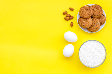 Fototapeta na wymiar Ingredients for homemade cookies. Fresh cookies near flour, eggs on yellow background top view copy space