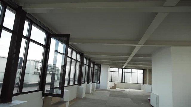 Camera shows Large empty room with cute big black framed windows, grey floor and white walls and ceiling without any furniture and people in daylight.