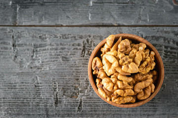Pieces of peeled walnut in a wooden bowl on a dark wooden table. The view from the top.