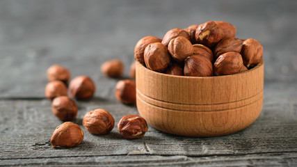 Wooden bowl with hazelnuts isolated on a black wooden table.
