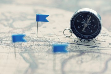 Compass and flag pins on blur vintage world map, journey concept