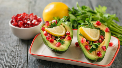 Avocado with pomegranate seeds, balsamic sauce, lemon and herbs on the table. Vegetarian cuisine for weight loss.