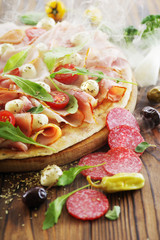 Fototapeta na wymiar Hot pizza with smoke, close-up with prosciutto ham, mozzarella, cherry tomatoes and various ingredients.
