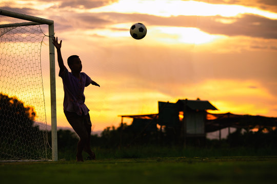 An action sport picture of a kids playing soccer football as a goalkeeper for exercise in community rural area under the sunset.