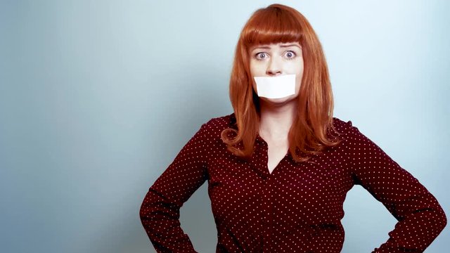 Redhead woman in polka dot shirt with white tape over mouth