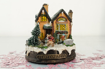 Christmas toy house with candy cane confetti against white background. Village little house figurine. Christmas decoration