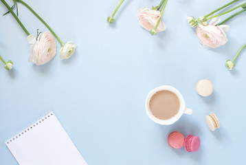Flowers background. Pastel colors pink ranunkulus flowers, cup of cocoa, macaroni cakes , notebook on pale blue background. Top view.Copy space