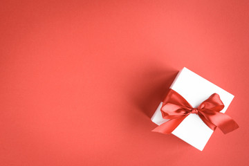 Gift box with red ribbon bow on red background.