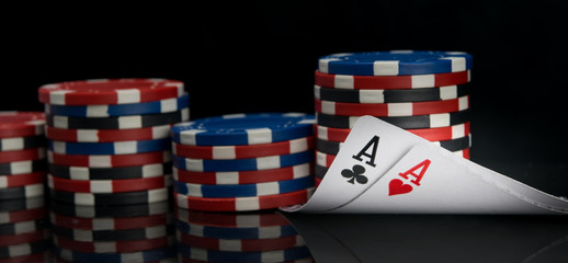 the combination of two aces is reflected on the surface of the black background, surrounded by the chips of a large bet for poker