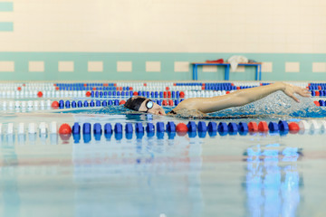 Young woman in goggles and cap swimming front crawl stroke style in the blue water indoor race pool