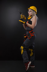 girl in construction clothes and protective equipment posing with a screwdriver