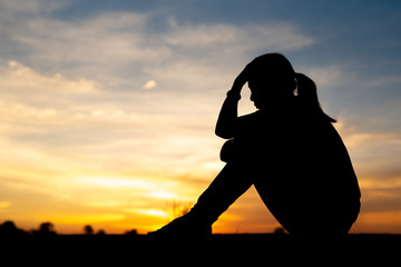 Silhouette of sad and depressed women sitting at walkway of park with sunset