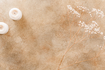 Top view on a beige stone textured background with dried plant and white candles. Flat lay, place for text.