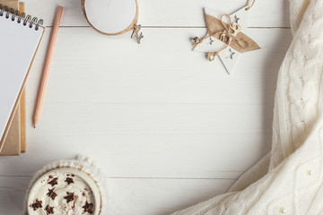 A cup of hot winter drink, with whipped cream and powder with an asterisk, a notebook, white snowflakes and a knitted scarf on a wooden table. Christmas concept in bright colors. Copy space.