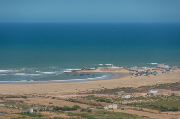 Panoramic view to waves on Atlantic ocean coastline and fisherman's village with blue boats. Morocco