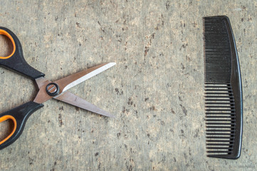 A scissors and a comb kept on a grey wooden textured table top view