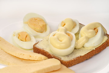 Bread sandwich with buttered eggs with mayonnaise and cheese on a white plate and white background, close-up