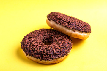 Two delicious chocolate donuts with sprinkle on bright yellow background