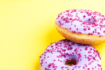 Two delicious lilac donuts with sprinkle on bright yellow background
