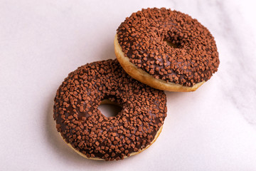 Two delicious chocolate donuts with sprinkle on light marble background