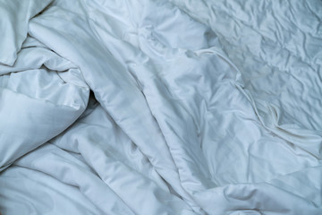 White linen blanket in hotel bedroom. Close up detail of messy white blanket after waking up in morning. Comfortable bed with soft white duvet. Sleep tight with good quality bedding household concept.