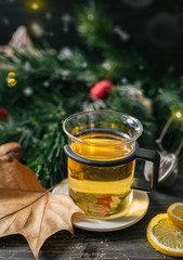 cup of tea on wooden rustic table with christmas decorated blurred pine tree leaves in background