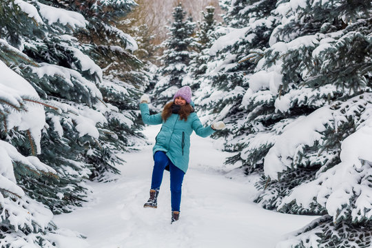 young happy excited woman in knitted hat and blue down jacket throws snow in spruce forest, winter happy portrait, holiday Christmas vibes