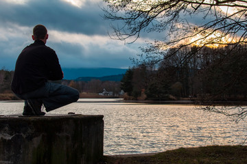 Fototapeta premium Silhouette of young man sitting on outlet of pond