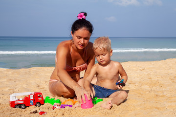 beautiful mom brunette is playing with her son blonde against a blue sky on the beach