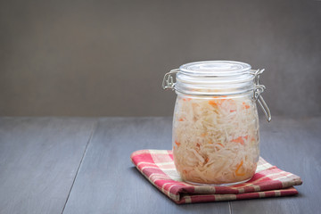 Homemade sauerkraut, marinated cabbage salad in a glass jar on wooden table.  Fermented healthy vegetarian food concept. Copy space.