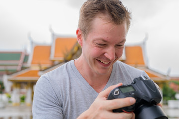 Face of happy tourist man checking camera against view of the Buddhist temple in Bangkok