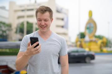 Young happy tourist man using phone against Ratchadamnoen street in Bangkok