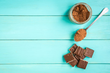 Milk chocolate bar and cocoa on blue wooden background.