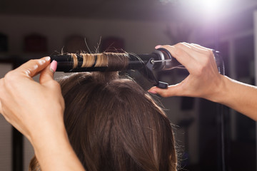 professional hairdresser making a hair curling to a client with long hair in a beauty salon. concept of stylist training - obrazy, fototapety, plakaty